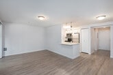 This single-floor unit offers a thoughtfully designed open-concept layout that seamlessly connects the kitchen and living area, creating a bright and functional living space. The kitchen is a standout feature, equipped with stainless steel appliances including a range, microwave, refrigerator, and dishwasher. White shaker-style cabinetry provides ample storage, while a green glass tile backsplash adds a touch of color and texture. Light-toned quartz countertops extend across the kitchen and wrap around a peninsula, which serves as both a prep area and casual dining space. Stylish pendant lights with geometric glass shades hang above the peninsula, adding a contemporary accent to the space. The living area is finished with warm wood-tone laminate flooring that runs throughout the main areas, complemented by neutral walls that contribute to a clean, modern aesthetic. A sliding glass door and adjacent window allow natural light to flow in while providing views of the surrounding greenery and access to an outdoor area. The bathroom is well-appointed with a white vanity featuring cabinet storage, a large mirror, and light wood-tone flooring that maintains consistency with the rest of the unit. Overall, this space presents a cohesive, updated interior with practical design choices suited for comfortable everyday living.