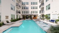 This contemporary residential community is designed with both style and functionality in mind. At its heart lies a striking courtyard pool, framed by the building's clean white modern façade, black iron railings, and private balconies. The pool area features ample lounge seating, large decorative planters with lush greenery, and a relaxed outdoor ambiance ideal for unwinding.

The common areas inside reflect the same modern aesthetic, with light wood-look flooring, crisp white walls, and carefully curated artwork adding warmth and character to the corridors. Natural light filters through glass-paneled doors, connecting interior spaces to the outdoors seamlessly.

Residents benefit from a well-appointed fitness center, visible through floor-to-ceiling glass doors and equipped with cardio machines, free weights, a weight rack, and stability equipment—catering to a full range of workout needs.

Package management is handled efficiently through an Amazon Hub locker system, conveniently located near the building entrance alongside traditional mailboxes. The overall design of the community prioritizes a clean, upscale atmosphere, combining practical amenities with thoughtful architectural details to create a polished and comfortable living environment.