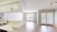Located in Aventura, FL, this one-bedroom, one-bathroom residence offers a well-designed single-floor layout with a clean, contemporary aesthetic throughout. Wood-look flooring flows seamlessly across all living areas, complementing the neutral warm-gray wall tones and crisp white trim that define the interior palette.

The open living room is a comfortable, airy space anchored by a ceiling fan with light fixture and a set of sliding glass doors that lead to a private balcony overlooking the pool — filling the room with natural light and lush outdoor views. An open pass-through connects the living area to the kitchen, which features white shaker-style cabinetry with crown molding detail, light quartz countertops, a stone tile backsplash, and stainless steel appliances including a refrigerator, dishwasher, and range. A window above the sink brings in additional natural light.

The bedroom is a well-proportioned retreat with large windows framing views of swaying palm trees, offering a serene Florida backdrop. The bathroom is clean and functional, finished with wood-look tile flooring, a white tub-shower combo with tile surround, and a light quartz vanity countertop. Throughout, the space maintains a bright, move-in-ready feel suited to the South Florida lifestyle.