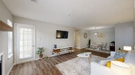 This single-floor residence offers a practical and well-designed layout across two bedrooms and two bathrooms. The open-concept living, dining, and kitchen area forms the heart of the home, featuring warm wood-look vinyl plank flooring throughout. The living room is highlighted by a fireplace with a rustic wood mantel, vaulted ceilings, and a glass door that allows natural light to fill the space. The dining area flows seamlessly from the living room, illuminated by a pendant light fixture overhead. The kitchen is equipped with gray cabinetry, light stone countertops, stainless steel appliances including a refrigerator and range, and a classic white subway tile backsplash, with a window overlooking the outdoors. Both bedrooms feature plush carpet flooring and natural light from windows. The primary bedroom is generously sized, complete with a ceiling fan, while the second bedroom includes a glass door for additional light. Each bathroom is finished with gray vanity cabinetry, stone-look countertops, wood-look flooring, and a tiled tub-shower combination. A dedicated in-unit laundry room houses a full-size washer and dryer with overhead shelving, adding everyday convenience to this thoughtfully designed home.