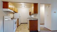 This single-floor unit offers a practical and straightforward layout connecting several well-defined living spaces. The kitchen is designed for efficiency, featuring warm-toned wood cabinetry both above and below the counters, a granite-look countertop with an integrated sink, a white electric range, a refrigerator, and a dishwasher. Durable tile flooring runs throughout the kitchen, providing a clean transition into the adjacent living area. The living room is spacious and carpeted, with a textured ceiling and an open sightline into the kitchen, creating a connected, open feel. Natural light filters into the space through a window dressed with vertical blinds.

The bedrooms are carpeted and bright, each featuring windows with vertical blinds that allow natural light in, ceiling fans for added comfort, and baseboard heating along the walls. One bedroom includes a walk-in closet with built-in shelving, offering generous storage. The bathroom is finished with classic white square wall tile surrounding a full tub-shower combo, mosaic tile flooring, a wood-trimmed vanity, and a window above the tub that brings in natural light. Overall, the unit presents a clean, functional living environment.