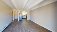 This single-floor residence offers a well-organized and functional layout with a cohesive design throughout. The open living and dining area is anchored by distinctive exposed beam ceilings with a textured finish, and durable wood-look flooring that extends seamlessly into the kitchen. The kitchen is efficiently designed in a U-shaped configuration, featuring white cabinetry, light countertops, a tile backsplash, and a full suite of stainless steel appliances including a refrigerator, gas range, dishwasher, and microwave. A window above the sink allows natural light to brighten the workspace. The bedrooms are finished with plush carpeting and ceiling fans with integrated lighting, providing a comfortable retreat. One bedroom includes a sliding glass door that opens directly onto a private balcony, offering pleasant outdoor views and natural light. Baseboard heating is present throughout for efficient climate control. The bathroom features a white vanity with a light stone-look countertop, a framed mirror with overhead vanity lighting, and a separate tub and shower area with a bright window. The overall aesthetic is clean and neutral, creating a versatile and move-in-ready living environment.
