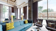 This elegantly designed lounge space makes an immediate impression with its soaring double-height ceilings and dramatic floor-to-ceiling windows that flood the interior with natural light and offer views of the surrounding greenery. A coffered ceiling detail anchors the space overhead, adorned with a striking geometric chandelier crafted from open metalwork and warm Edison-style bulbs, adding an industrial yet refined touch to the refined atmosphere.

The interior design palette balances neutral tones with bold accents. Textured dark wall panels provide a sophisticated backdrop, complemented by flowing floor-length curtains in muted taupe that frame the expansive windows. Seating is thoughtfully arranged to encourage conversation and relaxation, centered around a vibrant teal leather sofa accented with vivid yellow-green floral cushions. A sculptural dark grey swivel chair adds an additional seating option with an artistic flair.

Paired table lamps with gold bases and white shades provide warm ambient lighting, while a mirrored wall element visually expands the room and reflects the natural light throughout. The flooring features large-format light tiles, contributing to the open and airy feel of the space. Overall, this lounge exudes a contemporary, upscale ambiance with a carefully curated mix of textures, bold color pops, and architectural detail.