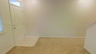 This two-story home in Fort Bragg, North Carolina, presents a straightforward and functional layout well-suited for a variety of living arrangements. The interior reflects a clean, neutral aesthetic, with light beige walls and matching carpet flooring that create a cohesive and understated look throughout. The room pictured features wall-to-wall carpeting in a warm tan tone, transitioning to tile flooring near the entryway — a practical detail that helps distinguish high-traffic zones from living areas. White baseboard trim lines the perimeter of the room, complementing the crisp white door and adding a polished finishing touch to the space. The walls are painted in a soft, neutral tone that allows for flexible decorating options. A single electrical outlet is centrally placed along one wall, and the overall layout of the room provides an open, unobstructed floor plan. The two-story structure offers separation between living and private spaces across floors, a common and practical feature for both individuals and families. The home's clean condition and neutral palette make it a versatile and move-in ready option for those stationed at or near Fort Bragg.