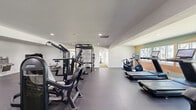 Located at 444 Saratoga Ave in Santa Clara, California, this fitness facility is thoughtfully divided into two distinct exercise rooms, together offering a comprehensive workout experience across a generous single-floor footprint. The main strength and cardio room features durable rubber flooring, recessed lighting, and full-length mirrors that enhance the sense of space. It is outfitted with a row of treadmills and ellipticals equipped with digital screens, Xebex rowing machines, a multi-station cable machine, a power rack, and a dedicated dumbbell rack with storage shelving. A built-in water fountain adds convenience for users. The second room is a bright, functional training space distinguished by its turf flooring and walls of floor-to-ceiling windows that invite abundant natural light and views of the surrounding greenery. This area is equipped for dynamic training with a ceiling-mounted suspension and pull-up rig, medicine balls, resistance tools, a stationary air bike, and a functional trainer. Clean white walls and a well-organized layout across both rooms create an inviting, professional atmosphere suited for a wide variety of fitness routines, from high-intensity interval training to steady-state cardio and strength work.