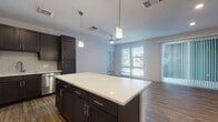 This thoughtfully designed single-floor residence combines modern finishes with a functional open-concept layout. The kitchen serves as a central highlight, anchored by a large white-topped island illuminated by stylish pendant lighting. Dark espresso cabinetry contrasts beautifully against a classic white subway tile backsplash, while a full suite of stainless steel appliances — including a refrigerator, range, microwave, and dishwasher — provides a polished, contemporary feel. Wood-style plank flooring flows seamlessly throughout the kitchen and living areas, enhancing the warm, cohesive aesthetic.

The open living area benefits from generous natural light streaming in through large windows fitted with blinds, and a ceiling fan adds both comfort and style. A built-in shelving nook off the main living space offers practical storage and display options.

The bedroom is generously sized and features plush wall-to-wall carpeting, large windows, and direct access to a walk-in closet with built-in shelving for ample organization.

The bathroom is clean and bright, finished with light-toned tile flooring, a tub-shower combination with white subway tile surround, a dark-cabinet vanity with white countertop, and open built-in shelving for additional storage. The overall ambiance throughout is modern, neutral, and move-in ready.