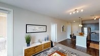 Located at 4001 Reedybrook Xing in Apex, NC, this single-floor residence offers a well-designed living environment with a clean, contemporary aesthetic. The open-concept layout connects the living area seamlessly to the rest of the home, creating a sense of spaciousness and ease of movement throughout.

The living area features warm hardwood-style flooring that transitions into plush carpeting, adding comfort underfoot. Neutral, light-toned walls provide a bright and welcoming ambiance, complemented by recessed and track lighting that ensures ample illumination throughout the day. The space is thoughtfully appointed, with room for stylish furnishings and décor that enhance the modern character of the home.

A glimpse toward the kitchen reveals bar-height seating at a countertop island, suggesting a practical and social dining setup ideal for everyday living or entertaining. White cabinetry and clean lines carry the contemporary design language into this functional area.

Interior doorways lead to additional rooms, offering a well-structured floor plan with defined spaces while maintaining an open and airy feel. The overall ambiance is modern and inviting, with attention to detail visible in the finishes and layout, making this Apex residence a comfortable and stylish place to call home.