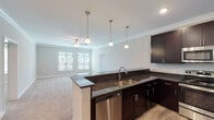 This single-floor residence is designed with a cohesive, modern aesthetic that carries consistently throughout each room. The kitchen serves as a central feature, showcasing rich dark espresso cabinetry paired with dark granite countertops and a full suite of stainless steel appliances, including a refrigerator, range, microwave, and dishwasher. A peninsula with pendant lighting above extends the counter space and opens directly to the living area, which is finished with plush carpeting, crown molding, and a ceiling fan. Natural light filters in through multiple windows fitted with blinds. A dedicated pantry with wire shelving provides substantial storage adjacent to the kitchen. The bedrooms are generously proportioned, each featuring soft carpet, ceiling fans, and windows that bring in natural light. The primary bedroom connects to an en-suite bathroom equipped with a dark vanity, granite countertop, a walk-in glass shower, and tile flooring. A second full bathroom mirrors the design language, featuring a matching vanity, a tub-shower combination, and a tall linen storage cabinet. A carpeted walk-in closet with wire shelving completes the primary suite. Crown molding and consistent finishes unify the space throughout.