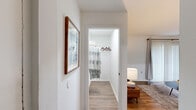 This single-floor residence offers a thoughtfully designed layout encompassing two bedrooms, two bathrooms, a combined living and dining area, a fully equipped kitchen, a closet, and a hallway. The open-plan living and dining space is finished with warm wood-tone flooring throughout, complemented by clean white walls that create a bright and welcoming atmosphere. Large sliding glass doors in the living room invite generous natural light and provide direct access to a private balcony with outdoor views. The kitchen features white shaker-style cabinetry with matte black hardware, white countertops, and stainless steel appliances including a gas range, built-in microwave, and a full-size refrigerator. The dining area accommodates a comfortable seating arrangement and is enhanced by a full-length mirror that amplifies the sense of space. The primary bedroom is a well-proportioned retreat with plush carpeting and soft, neutral tones. The second bedroom offers similarly comfortable proportions with vaulted ceiling detail and carpet flooring. The two bathrooms are clean and functional — one featuring a shower-tub combination, and the other presenting a vanity with a white countertop. Together, these spaces form a cohesive, move-in-ready home with a modern and practical design sensibility.