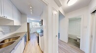 Located on the 8th floor at 250 Roehampton Avenue in Toronto's midtown neighbourhood, this thoughtfully designed suite offers a clean, modern aesthetic throughout its single-floor layout. The galley-style kitchen is a functional highlight, featuring white cabinetry, subway tile backsplash, dark countertops, stainless steel appliances including a built-in microwave, electric range, and dishwasher, all set above warm light wood-toned flooring. Recessed track lighting illuminates the kitchen corridor, which connects efficiently to the rest of the unit. The living area is bright and airy, benefiting from a window that frames views of the surrounding cityscape, with a baseboard heating unit running along the exterior wall. The bedroom is a clean, neutrally finished space with the same light hardwood-style flooring and crisp white walls, offering a calm and versatile environment. The bathroom is finished to a high standard, showcasing classic white subway tile surrounding a full soaker tub with an overhead shower, complemented by stone-look floor tiles and a clean white vanity. Throughout the unit, consistent use of white walls, light flooring, and modern fixtures creates a cohesive, bright, and contemporary living environment.