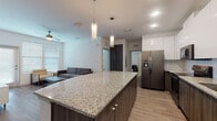 Located at 9010 Running Bull Rd in Orlando, Florida, this single-floor residence offers a clean, contemporary design with thoughtfully selected finishes throughout. The open-concept kitchen and living area serves as the heart of the home, anchored by a large granite-topped island with pendant lighting overhead. The kitchen is equipped with stainless steel appliances, including a French door refrigerator, electric range, microwave, and dishwasher, complemented by high-gloss white upper cabinetry and dark wood-toned lower cabinets with a subway tile backsplash. Wood-look plank flooring flows seamlessly through the main living areas, adding warmth and continuity. The living room is generously proportioned, featuring a ceiling fan, large windows with blinds that invite abundant natural light, and direct access to an exterior door. The bedrooms are carpeted for comfort, each offering multiple windows and access to closet space. The bathroom is finished with earthy taupe tile surrounding a soaking tub and shower combination, set against light porcelain floor tiles. Throughout the home, a neutral color palette, recessed lighting, and modern fixtures contribute to a bright, cohesive, and move-in-ready atmosphere.