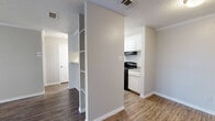 This well-organized one-bedroom, one-bathroom unit offers a practical and comfortable single-floor layout spanning a compact yet efficient footprint. The combined living, dining, and kitchen area forms the heart of the home, featuring wood-look hardwood-style flooring that runs throughout the main living spaces. A built-in open shelving unit serves as a stylish partial divider between the living and kitchen areas, adding both character and functional display space. Crown molding accents the living area, lending a touch of architectural detail to the space.

The galley-style kitchen is efficiently designed with white cabinetry, granite-style countertops, and black appliances including a range, oven, and refrigerator, all complemented by a stainless steel sink and under-cabinet range hood.

The bedroom is carpeted for comfort and features a window with blinds that allow for natural light. It provides access to a generously sized walk-in closet equipped with built-in shelving and multiple hanging rods, offering ample storage. A second closet provides additional storage convenience.

The bathroom includes a full tub-shower combination, a white vanity with granite-style countertops, a large mirror, and wood-look flooring. Textured ceilings are present throughout the unit, consistent with the overall design aesthetic.