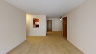 This single-floor unit at 10761 Smetana Rd in Minnetonka, Minnesota offers a functional and straightforward layout across a well-organized floor plan. The living area is generously sized, featuring neutral-toned carpet, a textured ceiling, and a large sliding glass door that fills the space with natural light and provides views of the surrounding greenery. A ceiling fan is also present, adding to the room's comfort. Adjacent to the living area, a pass-through opening connects to the kitchen, which is equipped with warm wood cabinetry, ample upper and lower storage, a double stainless steel sink, white countertops, and black appliances, including a dishwasher.

The bedrooms are carpeted and feature windows overlooking tree-lined outdoor scenery, with wall-mounted air conditioning units and baseboard heaters providing year-round climate control. The unit includes two bathrooms: one featuring hardwood-style flooring, a wood-framed mirror, a single vanity, and a tub-shower combination, and a second with white tile surround, a soaking tub, and chrome fixtures. Neutral wall tones and consistent finishes throughout the unit contribute to a clean, understated aesthetic well-suited for a variety of living arrangements.