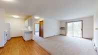 This Willowwood unit is a two-bedroom, one-bathroom residence laid out on a single floor, offering a clean and functional design throughout. The open living area features a combination of hardwood-style flooring and plush carpeting, with a wall-mounted air conditioning unit and a sliding glass door that opens to a balcony with views of surrounding greenery. Natural light flows in through the large glass door, brightening the main living space. The kitchen is efficiently designed with white cabinetry, a white countertop with a built-in sink, and white appliances including a refrigerator and range. A peninsula counter provides a natural division between the kitchen and living area, while an adjacent walk-in pantry or storage closet adds valuable organizational space. Both bedrooms are carpeted and feature windows with blinds that frame outdoor views, along with baseboard heating units for year-round comfort. The bathroom includes a full tub and shower combo with white tile accents, a vanity with under-sink storage, and a mirrored medicine cabinet. Throughout the unit, wood-toned door frames and trim provide a warm contrast to the neutral white walls, creating a cohesive and practical living environment.