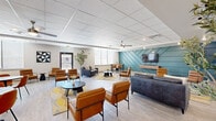 This well-appointed single-floor amenity space offers a thoughtfully designed layout across three distinct functional areas, providing residents with a versatile and inviting environment for socializing, relaxing, and gathering.

The centerpiece of the space is a spacious open lounge area featuring light wood-style flooring, a drop-panel ceiling with a ceiling fan, and abundant natural light from large windows fitted with blinds. A striking teal geometric accent wall serves as the focal point, anchoring a wall-mounted flat-screen TV above a media console. Comfortable seating includes a plush navy sofa and multiple cognac leather chairs arranged around modern coffee tables atop geometric-patterned area rugs.

The adjacent kitchen is sleek and functional, outfitted with gray shaker-style cabinetry, granite countertops, a center island with bar stools, a black refrigerator, dishwasher, and microwave. A teal accent wall with rustic floating wood shelves adds warmth and character, while generous windows maintain a bright atmosphere.

A dedicated screening room provides a true cinematic experience, with rows of leather recliner chairs, classic movie poster décor, and a teal accent wall, offering an intimate retreat for film enthusiasts.

Additional areas include a high-top communal dining table, smaller round tables for casual gatherings, and cozy nooks furnished with warm-toned chairs — creating a complete, community-focused space.
