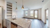 This single-floor unit showcases a contemporary design highlighted by wood-look plank flooring that runs consistently throughout the space, creating a cohesive and clean aesthetic. The kitchen serves as a central feature, equipped with stainless steel appliances including a refrigerator, range, microwave, and dishwasher. Granite countertops extend across both the perimeter cabinetry and a peninsula island, which is illuminated by a pair of brushed gold pendant lights. Gray shaker-style cabinetry provides ample storage, while open shelving adds functional display space. A stacked washer and dryer unit is conveniently tucked into a dedicated laundry closet directly off the kitchen.

The open-concept living area adjoins the kitchen seamlessly, benefiting from multiple windows and a glass door that invite natural light and offer outdoor views. A ceiling fan adds comfort to the living space.

The bathroom features granite vanity countertops with an undermount sink, gray cabinetry, and a full tub-shower combination with white tile surround. Directly accessible from the bathroom is a walk-in closet outfitted with built-in shelving and hanging rods, providing generous storage. The overall ambiance is bright, clean, and move-in ready.
