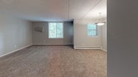 This single-floor unit offers a practical and comfortable layout designed for everyday living. The kitchen is a standout feature, outfitted with white shaker-style cabinetry, light countertops, and a full suite of stainless steel appliances including a dishwasher, electric range, and over-the-range microwave. Wood-look flooring adds warmth to the kitchen, and a window above the sink frames a view of surrounding greenery.

The living and bedroom areas are finished with plush wall-to-wall carpeting in a neutral tone, complemented by light gray walls that create a clean, cohesive aesthetic throughout. A drop-panel ceiling is featured in portions of the living area, while a textured ceiling carries through the remaining rooms. Baseboard heating runs along the perimeter of the carpeted rooms, and wall-mounted AC units provide additional climate control. Multiple windows invite natural light and offer pleasant views of the outdoors.

The unit includes two bathrooms, each finished with light tile flooring and white fixtures. Both bathrooms feature a vanity with storage cabinetry, a framed mirror, and a well-lit vanity light bar, keeping the spaces bright and functional. The floor plan, as seen in the dollhouse view, reveals a well-organized layout with clearly defined rooms and easy flow between spaces.