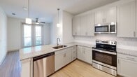 Located at 2600 Lakefront Trail in Rockwall, TX, this one-bedroom, one-bathroom residence offers a well-designed single-floor layout with a clean, modern aesthetic. The open-concept living area seamlessly integrates the kitchen, dining, and living spaces, creating an inviting and functional environment. The kitchen is a standout feature, equipped with stainless steel appliances including a refrigerator, electric range, microwave, and dishwasher. White shaker-style cabinetry with brushed nickel hardware pairs elegantly with granite countertops and a decorative patterned tile backsplash. A peninsula with an undermount sink provides additional prep space and casual seating potential. Light wood-style flooring runs throughout the main living areas, while pendant lighting adds a polished touch overhead. The bedroom is a comfortable retreat finished with plush carpet, a ceiling fan, and a window that fills the room with natural light. The bathroom features wood-look tile flooring, a soaking tub with white subway tile surround, a granite-topped vanity, and convenient access to a dedicated walk-in closet with built-in shelving. Two closets total provide ample storage. A private patio extends the living space outdoors, ideal for relaxing or taking in the surroundings.