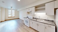 Located at 12370 SE Ash St in Portland, Oregon, this efficiently designed one-bedroom, one-bathroom unit offers a thoughtful layout across a single floor. The open-plan living, dining, and kitchen area forms the heart of the home, featuring light wood laminate flooring, crisp white walls, and recessed lighting that create a bright, clean aesthetic throughout. A ceiling fan adds comfort to the living area, which receives natural light through a street-facing window.

The kitchen is well-appointed with light gray cabinetry offering ample upper and lower storage, open display shelving, a dark laminate countertop, a stainless steel sink, an electric range, and a full-size refrigerator — all arranged along a single efficient wall.

The bedroom is a cozy, sun-lit room with a window overlooking greenery, light wood floors, and warm wood baseboards. It connects directly to a generously sized walk-in closet outfitted with wire shelving and hanging rods, providing excellent storage capacity relative to the unit's overall footprint.

The bathroom features a single-sink vanity with dark countertop, white cabinetry, a toilet, and a full shower/tub combination, all finished in a clean, neutral palette. Natural wood-trimmed doors throughout the unit add a warm, distinctive touch to the overall design.