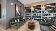 Located on Piedmont Road in Atlanta's prestigious Buckhead district, this single-floor commercial space offers a thoughtfully designed interior that blends elegance with functionality. The layout comprises two distinct areas, each finished to an exceptional standard.

The main lounge and bar area is a showpiece of contemporary design, anchored by a striking bar with a dark stone countertop, wood-paneled base with brass accents, and gold-toned bar stools. A decorative backsplash tile wall, wall-mounted TV, and an eye-catching constellation of brass ceiling fixtures lend the space a vibrant, upscale character. Light wood-look tile flooring runs throughout, complementing the neutral palette. Floor-to-ceiling windows flood the interior with natural light and provide direct views of the bustling Buckhead streetscape, framed by elegant white columns.

A separate lounge nook features a dramatic floor-to-ceiling built-in shelving unit with blue-paneled backing, brass wall sconces, and curated décor, accompanied by plush velvet seating. Adjacent to this is a private meeting or conference room with bold geometric patterned carpeting, custom cabinetry, a wall-mounted display, and large windows. A dining area with a solid wood table and a frosted-glass French door completes this versatile, design-forward space.