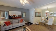 This single-story residence in Bellair, FL offers a thoughtfully designed layout with multiple living spaces finished in a warm, neutral palette throughout. The welcoming entryway opens into a carpeted living room accented by a textured ceiling, ceiling fan, and a sliding glass door that invites natural light and provides outdoor views. The living area transitions seamlessly from a defined entry zone to a relaxed seating space, creating a comfortable flow for daily living.

The kitchen features dark espresso cabinetry, light quartz-style countertops, and black appliances including a coil-burner range and full-size refrigerator, providing a practical and efficient cooking environment.

Two well-proportioned bedrooms offer plush carpeting, multiple windows with blinds and curtain panels for light control, and ample space for full bedroom furniture sets. Each room carries a distinct character — one with rich, dark wood furnishings and mirrored wall décor, the other with a lighter, contemporary aesthetic.

Two full bathrooms serve the home, each equipped with a shower-tub combination, vanity with light countertops, and wood-look flooring. The layout, as seen in the dollhouse view, provides a sensible separation of living and sleeping spaces, making this a functional and comfortable home in the Bellair area.