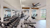 Located at 5026 Zion Rd in Garland, TX, this fitness center offers a thoughtfully designed, single-floor exercise facility that blends modern aesthetics with rustic architectural details. Exposed wooden ceiling beams contrast beautifully against crisp white painted brick walls and columns, creating a warm yet contemporary atmosphere throughout the space. Large black-framed windows invite abundant natural light, while multiple oversized ceiling fans ensure consistent airflow across the generously proportioned floor plan.

The main workout area is organized into distinct training zones. The strength zone features a full dumbbell rack, adjustable benches, and Matrix cable and multi-functional weight machines, all reflected in floor-to-ceiling mirrors that amplify the sense of openness. A dedicated cardio section houses a row of treadmills, stair climbers, ellipticals, stationary bikes, and rowing machines positioned near the windows for an energizing outdoor view. A separate functional training room provides additional space with medicine balls and a wall-mounted display screen, offering a quieter area for focused workouts.

The entry area showcases stylish slate-toned vertical tile accents, warm brass pendant lighting, and a built-in shelving unit with a marble countertop, setting an elevated tone from the moment of arrival. Neutral-toned carpet tiles and recessed lighting complete the polished, professional ambiance of this well-appointed fitness facility.