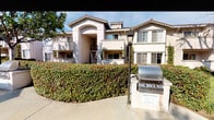 The courtyard at 1190 Encinitas is a thoughtfully designed outdoor common area that serves as a central gathering space within a residential community. The space is characterized by sweeping concrete pathways that wind through manicured green lawns, connecting various areas of the courtyard and providing easy access throughout the grounds. Mature deciduous and evergreen trees are strategically placed throughout, offering natural shade and a sense of established, park-like character.

A dedicated BBQ station, equipped with a stainless steel grill mounted on a built-in counter, is conveniently positioned near the pathways and bordered by well-trimmed hedgerows, making it ideal for outdoor dining and social gatherings. Adjacent to the grill area, a concrete picnic table with matching benches sits beneath a large market umbrella, providing a comfortable shaded spot for residents to relax and dine al fresco.

The surrounding multi-story residential buildings feature a Mediterranean-influenced architectural style, with stucco exteriors in warm neutral tones, tile rooflines, and balconies overlooking the courtyard. Classic lamp posts add a charming detail to the hardscaped areas. The overall ambiance is tranquil and inviting, with abundant natural light and well-maintained greenery enhancing the community atmosphere.