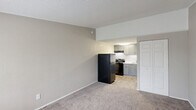 This updated studio in Augusta, Georgia offers an efficient, single-level layout encompassing a living area, kitchen, and full bathroom. The living space features neutral-toned carpet, textured walls, and a textured ceiling, creating a clean and understated atmosphere. A window near the entry door allows natural light to filter in, brightening the room, while a wall-mounted HVAC unit provides climate control. A white bi-fold closet door offers convenient built-in storage.

The kitchen flows seamlessly from the living area and is appointed with gray shaker-style cabinetry, brushed gold hardware, and a marble-look countertop that adds a modern touch. Black appliances — including a refrigerator, electric range, and range hood — complete the functional cooking space, while wood-look flooring ties the area together.

The bathroom continues the updated aesthetic with a gray vanity, white countertop, and a mirrored medicine cabinet above. Gold-toned towel and paper holders accent the textured walls, and wood-look tile flooring adds a cohesive, contemporary finish. The overall design of the space reflects thoughtful updates throughout, offering a practical and modern living environment.