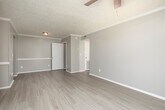 Located at 5856 Eagle Cir in Montgomery, Alabama, this single-floor home offers a clean, functional layout with neutral tones and updated finishes throughout. The living area is bright and open, featuring light-colored luxury vinyl plank flooring, textured ceilings with crown molding accents, and a sliding glass door dressed with vertical blinds that invites natural light into the space. A ceiling fan adds comfort, and the layout connects seamlessly to adjacent areas of the home. The galley-style kitchen is efficiently designed with white cabinetry, light countertops, a double basin sink, and black appliances including a refrigerator, providing ample storage and workspace. A secondary open area with matching LVP flooring offers flexibility as a dining room or additional living space, with a clear sightline into the kitchen. The bedroom features plush carpet flooring, soft neutral walls, a textured ceiling, and a window that brings in natural light. The bathroom is well-appointed with a white vanity, light countertop, large mirror, wall sconce lighting, and wood-look flooring. Throughout the home, consistent warm-gray wall tones and white trim create a cohesive, move-in-ready aesthetic.