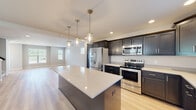 This well-appointed two-floor home combines modern design with practical functionality throughout its thoughtfully laid-out spaces. At the heart of the main level is an open-concept kitchen and living area, designed to encourage seamless flow between spaces. The kitchen is a standout feature, showcasing dark shaker-style cabinetry that reaches toward the ceiling, bright quartz countertops, and a generous central island that serves as both a prep space and a gathering point. A full suite of stainless steel appliances — including a French door refrigerator, electric range, over-the-range microwave, and dishwasher — completes the culinary space. Pendant lighting above the island and recessed ceiling lights add layered illumination throughout. Light-toned hardwood flooring runs through the main living areas, lending warmth and continuity to the open layout. The bedrooms offer plush carpeting underfoot and benefit from natural light through blinded windows, with ceiling fans providing year-round comfort. The bathroom features light hardwood flooring, a dark vanity with a single sink, and a tiled tub-shower combination. A half bath is also present for added convenience. The attached two-car garage provides ample storage and parking space, with an automatic opener already in place.