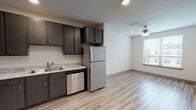 This well-appointed single-floor unit offers a thoughtful layout with modern finishes throughout. The open-concept kitchen flows seamlessly into the living area, creating a connected and functional space. The kitchen is equipped with a full suite of stainless steel appliances, including a refrigerator, dishwasher, range with oven, and microwave. Dark espresso-toned cabinetry extends from floor to ceiling, complemented by light granite-style countertops and a double-basin sink. Light wood-look luxury vinyl flooring runs throughout the kitchen and living areas, adding warmth and easy maintenance.

The living area benefits from natural light through a window fitted with blinds, and a ceiling fan provides year-round comfort. The bedroom is carpeted for added comfort and also features a ceiling fan and a window with views to the exterior. A spacious walk-in closet with built-in shelving and rod provides generous storage. Adjacent to the bedroom is a dedicated in-unit laundry area with a washer and dryer included.

The bathroom features matching dark cabinetry with a light countertop vanity, wood-look flooring, and a separate shower and toilet area. Throughout the unit, clean white walls, recessed lighting, and consistent modern hardware tie the design together cohesively.