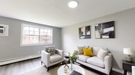 This well-appointed single-floor unit offers a cohesive, modern aesthetic throughout, with soft grey walls, light wood-tone vinyl plank flooring, and clean white trim creating a calm and contemporary atmosphere.

The inviting living room serves as the heart of the space, featuring a large window that fills the room with natural light and offers views of the surrounding neighborhood. The area provides generous room for comfortable seating arrangements, complemented by tasteful wall art and warm accent tones.

The kitchen is efficiently designed with crisp white shaker-style cabinetry, light quartz countertops, a classic subway tile backsplash, and a full suite of stainless steel appliances including a gas range and refrigerator. The layout maximizes functionality while maintaining a fresh, clean look.

The bedroom is a relaxing retreat, offering ample space and direct access to a well-sized closet equipped with a full-width shelf and hanging rod for convenient storage. Baseboard heating ensures year-round comfort.

The full bathroom is finished with large-format white floor tiles, light horizontal wall tiles in the tub surround, and a clean, minimalist design that emphasizes brightness and ease of maintenance. Every room reflects a consistent, updated finish that balances practicality with modern style.