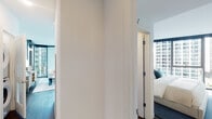 Located at 455 E Waterside Drive in Chicago's Streeterville neighborhood, this modern high-rise residence offers a thoughtfully designed single-floor layout with striking architectural details throughout. Floor-to-ceiling windows in the living room wrap around two sides, flooding the space with natural light and framing sweeping views of the Chicago skyline and surrounding greenery. The open living area features a clean, neutral palette with contemporary furnishings and a glass coffee table that complement the bright, airy atmosphere.

The kitchen is outfitted with sleek wood-toned cabinetry, crisp white upper cabinets, quartz countertops, a dark tile backsplash, and stainless steel appliances including a Bosch gas range with a built-in hood — ideal for serious home cooking.

The primary bedroom is distinguished by a bold teal accent wall, framed landscape artwork, and expansive floor-to-ceiling windows offering city and courtyard views. Its en-suite bathroom features a glass-enclosed walk-in shower, a wood-finish vanity with a large illuminated mirror, and large-format tile flooring. A second bedroom, also featuring a teal accent wall and floor-to-ceiling windows, includes a built-in desk area. The second bathroom offers a soaking tub with shower combination and a matching wood vanity.