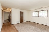 This single-floor residence offers a practical and straightforward layout across several rooms, as visible in the 3D floor plan. The living area features a combination of wood-look hard flooring and plush carpeting, with vertical blind-covered windows that allow natural light to filter in. A floor vent provides heating, and a dark-stained interior door adds a warm contrast to the cream-colored walls. The textured ceiling is a consistent feature throughout the space.

The kitchen is well-equipped with abundant dark wood cabinetry extending to the ceiling, a double-basin sink, a white refrigerator, dishwasher, and an electric range with overhead ventilation. Wood-look flooring and recessed lighting give the kitchen a functional, organized feel.

Multiple bedrooms are finished with wall-to-wall carpet, cream walls, dark baseboards, and individual windows fitted with horizontal blinds, providing a quiet and private atmosphere. One additional room features plain carpet and neutral walls, suitable for flexible use.

The bathroom includes a full-size soaking tub with an overhead shower, chrome fixtures, and wood-look flooring, offering a clean and utilitarian design.