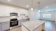 Located at 1300 S Davis Rd in LaGrange, Georgia, this well-appointed one-bedroom, one-bathroom residence offers a thoughtfully designed single-level layout with modern finishes throughout. The open-concept kitchen and living area serves as the heart of the home, anchored by a substantial granite-topped island illuminated by stylish pendant lighting. The kitchen is outfitted with stainless steel appliances—including a refrigerator, range, microwave, and dishwasher—complemented by crisp white upper cabinetry, gray lower cabinets, a subway tile backsplash, and a undermount sink. Light wood-look flooring extends throughout the main living areas, enhancing the bright, airy ambiance. The spacious bedroom features plush carpeting, a ceiling fan, and generous natural light from dual windows offering outdoor views. A dedicated closet provides ample storage. The bathroom mirrors the kitchen's refined aesthetic with granite countertops, gray cabinetry, a large vanity mirror, and wood-look flooring. A dedicated laundry room houses a full-size Whirlpool washer and dryer alongside overhead shelving, adding everyday convenience. Recessed lighting and neutral tones throughout create a clean, contemporary atmosphere well-suited for comfortable living.