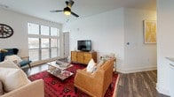 This single-floor, two-bedroom, two-bathroom residence offers a thoughtfully designed open-concept layout with distinct living, dining, and kitchen zones that flow seamlessly together. The kitchen is outfitted with white shaker cabinetry, granite countertops, a classic subway tile backsplash, and a full suite of stainless steel appliances, including a refrigerator, range, microwave, and dishwasher. A row of industrial-style pendant lights overhead adds a modern, urban touch. Rich, dark hardwood-style flooring runs throughout the main living areas, complementing the neutral white walls and creating a warm yet contemporary ambiance. The living room features large windows that invite abundant natural light and outdoor views, along with a ceiling fan for added comfort. Both bedrooms are carpeted and generously sized, each with walk-in closets and ceiling fans. The primary bedroom benefits from a large window with exterior views. The two bathrooms are well-finished, one featuring a glass-enclosed walk-in shower with white subway tile, and the other offering a full bathtub with matching tile surround. A hallway connects the private quarters, maintaining a clean, organized flow throughout the residence.
