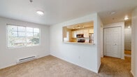 Located at 21167 NW Galice Ln in Portland, Oregon, this single-floor unit offers a clean, functional layout designed for comfortable everyday living. The open-concept living area is finished with plush wall-to-wall carpeting and connects seamlessly to the kitchen via a pass-through counter opening, creating a bright and connected space. Natural light filters in through windows that overlook the surrounding neighborhood. The kitchen is well-equipped with stainless steel appliances, including an electric range, over-the-range microwave, and refrigerator, all complemented by white cabinetry and light countertops. Track lighting illuminates the kitchen workspace effectively. The unit includes multiple bedrooms, each carpeted and featuring white panel doors and closet storage. A carpeted hallway with additional closet space connects the private areas of the home. Two bathrooms feature light hardwood-style flooring, white vanities with generous countertop space, large mirrors, and bright vanity lighting. One bathroom includes accessible grab bar features. A dedicated laundry room houses a full-size washer and dryer with overhead wire shelving for added storage. Baseboard heating is present in select rooms, and the overall interior presents a bright, neutral palette throughout.