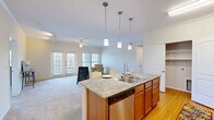 Located at 14220 S Wayside Dr in Houston, TX, this single-floor, 3-bedroom, 2-bathroom home offers a well-designed open-concept layout ideal for comfortable everyday living. The kitchen is a standout feature, equipped with stainless steel appliances including a refrigerator, stove, and dishwasher, complemented by warm wood cabinetry and granite countertops. A central island with pendant lighting doubles as a dining and prep space, and hardwood flooring runs throughout the kitchen area. The kitchen flows seamlessly into the combined living room, where plush carpeting, crown molding, a ceiling fan, and direct access to an outdoor balcony via French doors create an inviting and airy atmosphere. Natural light fills the living space through multiple windows. The bedrooms are carpeted and accented with crown molding and ceiling fans, offering a comfortable retreat. The primary bedroom connects to a dedicated closet and a private bathroom featuring wood cabinetry, a large vanity mirror, and hardwood flooring. A second full bathroom serves the remaining bedrooms. A hallway with closet access connects the rooms efficiently. Overall, the home presents a clean, functional design with consistent finishes throughout.
