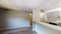 This single-story residence offers a practical and well-organized layout across several distinct living areas. The open living area is finished with wall-to-wall carpet and neutral gray walls, creating a clean and versatile space. A half-wall partition separates the living area from the kitchen, which features stone-look countertops, white cabinetry, and a full suite of black appliances including a refrigerator, range, over-the-range microwave, and dishwasher. The kitchen is finished with tile flooring, providing easy maintenance underfoot.

The bedrooms are carpeted and feature neutral wall tones, with one bedroom offering direct access to a private bathroom and closet storage. Closets include built-in shelving and hanging rods. Natural light enters through windows fitted with horizontal blinds. The bathrooms are equipped with granite-style vanity countertops, gray cabinetry, large mirrors, and towel bars. One bathroom includes a tub-shower combination with a curtain rod, while the other is similarly appointed. Ceiling vents throughout provide consistent climate control. The overall design is clean and functional, with consistent finishes carried throughout the home.