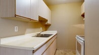 This single-floor, one-bedroom, one-bathroom unit in Inkster, Michigan offers a straightforward and functional layout. The living area is carpeted in gray and features a full-length sliding glass door dressed with vertical blinds, allowing natural light to fill the space while providing outdoor views of the surrounding grounds. A wall-mounted air conditioning unit and perimeter baseboard heating ensure year-round climate control. An additional window in the living area further supplements natural light.

The kitchen is equipped with white laminate cabinetry, a double-basin sink, white countertops, and tile flooring. Upper and lower cabinet storage offers practical organization space, and a white appliance is included. The layout is compact and efficiently arranged.

The bedroom is a well-proportioned, carpeted room with a window fitted with horizontal blinds that brings in natural light. Baseboard heating lines the wall, and an open doorway connects to the adjacent hallway.

The bathroom features a full-sized soaking tub with white subway tile surround, a chrome faucet, and a standard toilet. Mosaic tile flooring adds a classic touch. Neutral beige tones are consistent throughout the unit, contributing to a clean, understated aesthetic overall.
