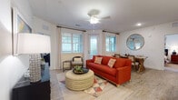 Located at 103 Inspiration Ave in Bluffton, South Carolina, this single-floor residence offers a thoughtfully designed layout that blends comfort and functionality. The open-concept living area features durable wood-look flooring, a ceiling fan, and an abundance of natural light streaming through multiple windows dressed with stylish grid-patterned curtains and blinds. The space flows seamlessly into the dining area, which is anchored by a rustic wooden dining table and accented by a large round gold-framed mirror. The kitchen is outfitted with crisp white beadboard cabinetry, granite countertops, stainless steel appliances, and a built-in desk area — ideal for working from home. The bedroom provides a serene retreat with plush carpeting, a ceiling fan, natural light from well-dressed windows, and ample closet space with built-in shelving. Two full bathrooms feature granite vanity countertops, white cabinetry, and tub-shower combinations. Throughout the residence, a consistent use of wood-look flooring, white walls, and granite surfaces creates a cohesive, clean aesthetic that is both welcoming and easy to maintain.