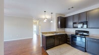 This well-appointed single-story home in Bowling Green, Kentucky offers three bedrooms and two full bathrooms within a thoughtfully designed floor plan. The open-concept kitchen and living area forms the heart of the home, where rich hardwood flooring flows seamlessly from the living room into the kitchen. The kitchen is equipped with dark espresso cabinetry, granite-style countertops, a peninsula with an undermount sink, pendant lighting, and black appliances including a range, microwave, dishwasher, and refrigerator. The living room features crown molding, a ceiling fan, and French doors that invite natural light and provide outdoor access. A dedicated utility room adds functional convenience. The bedrooms are carpeted and offer generous closet space, including walk-in and bi-fold closet configurations. The primary bedroom is comfortably sized with its own closet access. Both bathrooms are finished with tile flooring, dark vanity cabinetry, white countertops, and tub-shower combinations with oil-rubbed bronze fixtures. Connecting hallways are bright and clean, finished with crisp white trim and panel doors. The neutral color palette and consistent finishes throughout create a cohesive, move-in-ready living environment.