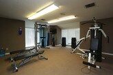 Located at 4133 Shoreline Cir in Virginia Beach, VA, this single-floor fitness space is purpose-built for comprehensive strength and conditioning training. The room is finished with neutral gray walls, wall-to-wall carpeting, and a textured ceiling equipped with overhead fluorescent lighting that ensures consistent, even illumination throughout the space.

The fitness area is well-appointed with a diverse array of professional-grade equipment. A Matrix functional trainer cable machine serves as a centerpiece near the windowed wall, complemented by a multi-station weight machine, adjustable benches, and a full rack of dumbbells for versatile free-weight training. A wall-mounted television and a standing water cooler add convenience and comfort to the workout environment.

A large floor-to-ceiling mirror spans one full wall, creating a sense of expanded depth while allowing users to monitor their form during exercise. Multiple windows fitted with horizontal blinds bring in natural light, further enhancing the open and energetic atmosphere of the room. The generous open floor space allows for free movement, stretching, and additional exercise routines beyond stationary equipment. The layout is thoughtfully organized to maximize functionality, making this a well-equipped and practical private fitness facility.
