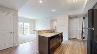 Located at 6160 Hall Rd in Galloway, Ohio, this single-floor, 3-bedroom, 2-bathroom home offers a thoughtfully designed layout with a clean, modern aesthetic. The open-concept kitchen and living area serves as the heart of the home, featuring a central island with light granite countertops, a double sink, and dark espresso cabinetry paired with black appliances. Wood-look flooring runs throughout the kitchen and living space, while recessed lighting adds a bright, polished finish. The living room extends naturally from the kitchen and opens to a private balcony through a sliding glass door, offering outdoor views of the surrounding community. Bedrooms are carpeted for comfort, including a generously sized primary bedroom with an ensuite bathroom featuring tile flooring and a glass-enclosed walk-in shower, plus a spacious walk-in closet with wire shelving on both sides. Additional bedrooms are well-sized with natural light from windows and ample closet space. A hallway connects all rooms efficiently, with dedicated laundry and utility rooms adding practical convenience. Eight closets throughout the home ensure exceptional storage capacity, making this a highly functional and comfortable living space.