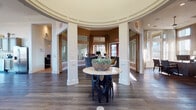 This elegantly designed single-floor community facility makes a striking first impression with its grand rotunda entryway, where a coffered circular ceiling crowns a dramatic focal point — a sculptural black pedestal table topped with a marble surface and a lush botanical centerpiece. Rich dark hardwood flooring flows throughout the entire space, anchoring the refined aesthetic.

The expansive lounge area offers generous seating arrangements centered around a stone-accented fireplace with a mounted flat-screen television. Soaring ceilings with clerestory windows invite abundant natural light, while ceiling fans and tasteful artwork, including a bold equestrian print, lend the room a polished, upscale character.

Adjacent to the lounge, a well-appointed leasing or administrative office features dual workstations, warm accent walls with textured wallcovering, large windows with flowing drapery, and ample natural light. A dedicated business center provides multiple computer workstations, built-in shelving, and pendant lighting, offering a functional and organized workspace.

The kitchen is fully equipped with taupe cabinetry, a mosaic tile backsplash, stainless steel appliances, and a large island with bar seating — ideal for community gatherings. Throughout, the space balances sophisticated design with practical amenities.