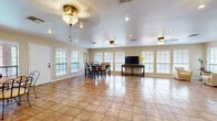 This well-appointed two-floor property offers a generous layout across two levels, with the main floor comprising the majority of the living space. Throughout the interior, warm terra-cotta ceramic tile flooring ties each room together, creating a cohesive and easy-to-maintain aesthetic.

The expansive main living area is anchored by a large sectional leather sofa and opens seamlessly toward a kitchen with light wood cabinetry and a breakfast bar. Ceiling fans and recessed lighting are featured throughout, complementing the abundant natural light that pours in through numerous windows fitted with plantation-style shutters.

A spacious dining area accommodates a tall pub-style dining table with seating for six, making it well-suited for gatherings. An adjacent sitting room offers a quieter retreat, furnished with accent chairs and decorative wall art.

The game room is a standout feature, centered around a full-size pool table beneath a pendant light, with additional wall art and built-in storage nearby. The dedicated fitness room is equipped with multiple cardio machines, floor-to-ceiling mirrors, a textured accent stone wall, and ample natural light from a row of windows.

The lower level provides supplementary space, rounding out this versatile and functional property ideal for both everyday living and entertaining.
