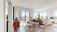 This thoughtfully designed 2-bedroom, 1-bathroom residence offers a bright and contemporary living experience across a single, efficiently organized floor. The open-concept living, dining, and kitchen area serves as the heart of the home, anchored by large floor-to-ceiling sliding glass doors that lead to a private balcony with sweeping city views. Natural light pours in from multiple oversized windows, complementing the light hardwood flooring found throughout.

The kitchen is outfitted with white shaker cabinetry, stainless steel appliances, a subway tile backsplash, and a quartz-topped island with bar seating. A built-in beverage center and open shelving niche add a refined, functional touch between the kitchen and living areas. The dining space benefits from a large picture window framing expansive city views.

The primary bedroom is a well-proportioned retreat with large windows and a ceiling fan, while the second bedroom mirrors the bright, airy aesthetic. The bathroom features a double vanity with LED-lit mirrors, a soaking tub, a glass-enclosed shower with subway tile, and marble-look flooring. A discreet hallway closet houses a stacked in-unit washer and dryer. Clean white walls, recessed lighting, and modern Shaker-style doors unify the space with a polished, contemporary character.