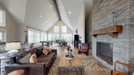 Located at 4890 Edwards Farm Rd in Hilliard, Ohio, this single-floor community clubhouse — known as "The Pointe" — offers an impressive blend of rustic warmth and modern design. The centerpiece of the space is a dramatic great room with soaring cathedral ceilings accented by exposed wooden beams and an abundance of recessed lighting. A floor-to-ceiling stacked stone fireplace with a solid wood mantel commands one wall, creating a cozy yet grand focal point. Wide-plank hardwood floors run throughout, complementing the natural, lodge-inspired aesthetic. Expansive windows and a set of full-glass entry doors flood the interior with natural light while offering views of the surrounding landscape. The open layout accommodates multiple functional zones, including a comfortable lounge area with leather seating, a game area featuring a pool table, and a leasing office with a reception desk and branded signage. A kitchenette is equipped with dark cabinetry, stone countertops, a stainless steel sink, and open wood shelving. A dedicated fitness center is enclosed by full-height glass partition walls, providing visibility and an airy feel. The overall ambiance is welcoming and well-appointed, designed to serve as a vibrant community hub.