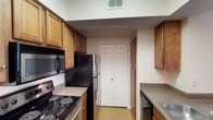 This two-floor space offers a practical and well-organized layout designed for comfortable everyday living. The kitchen is a standout feature, showcasing warm honey-toned wood cabinetry that extends to the upper walls, maximizing storage capacity. Equipped with a full suite of appliances — including a black electric range with coil burners, an over-the-range microwave, a refrigerator, and a dishwasher — the kitchen is fully functional and move-in ready. Speckled granite-style countertops provide ample prep space, complementing the rich cabinetry tones. Light hardwood-style flooring runs throughout, contributing to a bright and clean aesthetic. A ceiling HVAC vent ensures climate control throughout the space. Double bi-fold doors open to a closet, offering additional storage conveniently located just off the kitchen. The corridor layout of the kitchen connects efficiently to the rest of the home, promoting a smooth flow between spaces. Spanning two floors, the overall layout provides a sense of separation between living and private areas, making it a versatile and well-structured home suitable for a variety of lifestyles.