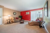 This single-floor, 2-bedroom, 1-bathroom residence offers a practical and comfortable layout across a compact yet efficient footprint. The living room is a standout space, featuring bold red accent walls, plush wall-to-wall carpeting, and a large sliding glass door that invites natural light and provides views of the surrounding greenery. The adjacent dining area is complemented by a sage green accent wall and overhead lighting, creating an intimate setting for meals. The galley-style kitchen is outfitted with dark wood cabinetry, dual-basin stainless steel sink, wood-toned countertops, and tile flooring, offering ample storage and functionality. The primary bedroom features a calming sage green accent wall, carpeted flooring, a window with natural light, and dedicated closet space. The second bedroom is bright and neutral, with carpet, a closet with bifold doors, and a baseboard heating unit. The shared bathroom includes a wide vanity with a light countertop, dark wood cabinetry, and a large mirror. Throughout the residence, warm carpet tones, tasteful color accents, and consistent use of baseboard heating contribute to a cozy, cohesive ambiance well-suited for comfortable everyday living.